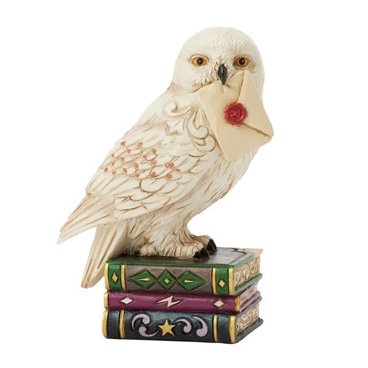 Mini figurine Hedwige Harry Potter by Jim Shore avec lettre de Poudlard posée sur des livres magiques colorés.